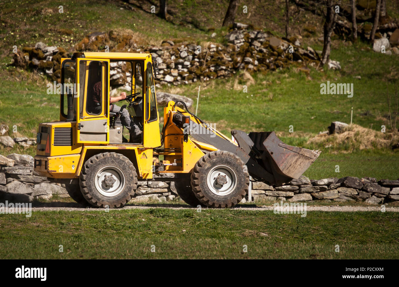 L'homme conduit une chargeuse-pelleteuse jaune dans une route de campagne Banque D'Images