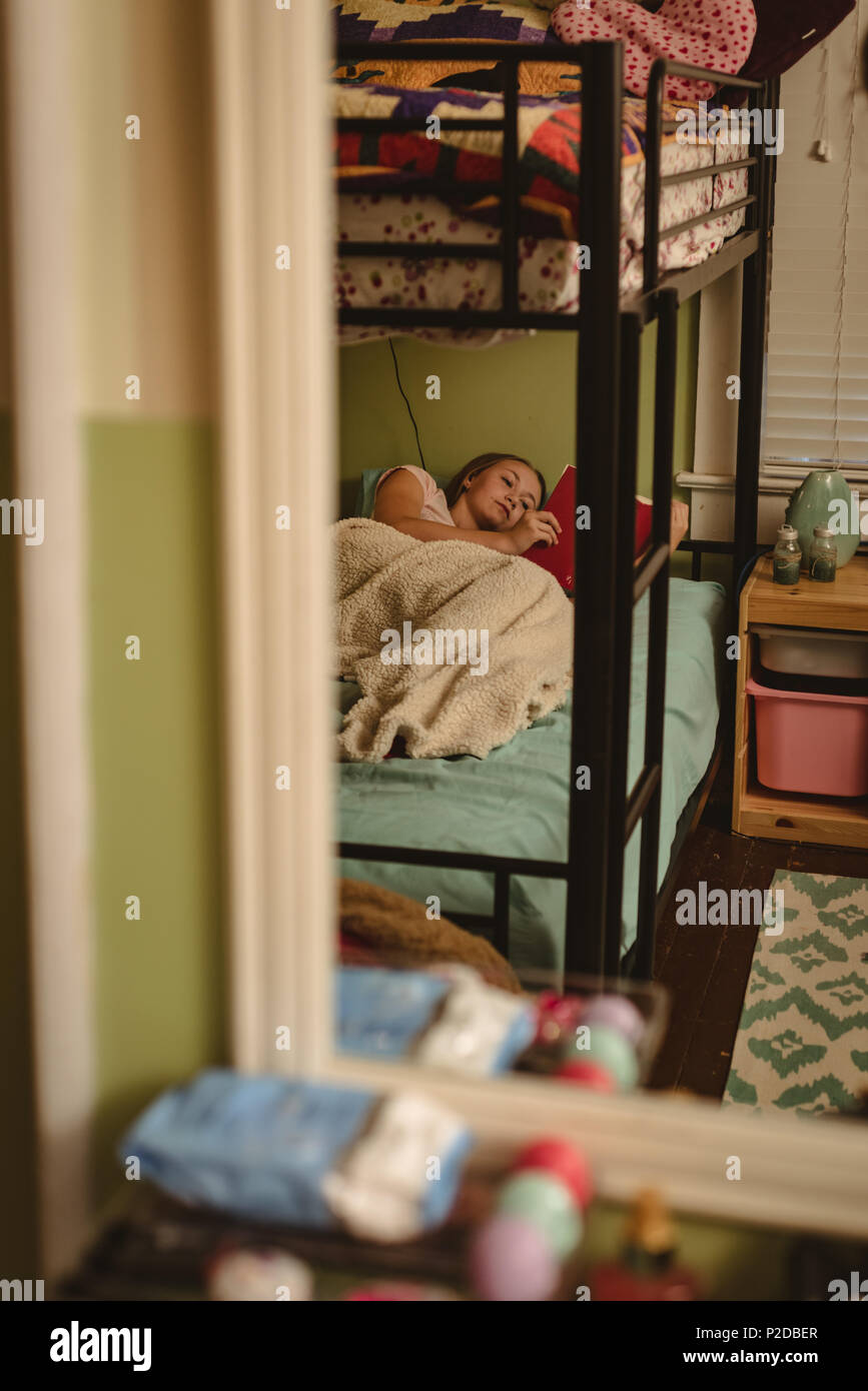 Girl reading a book while lying on lit dans la chambre Banque D'Images