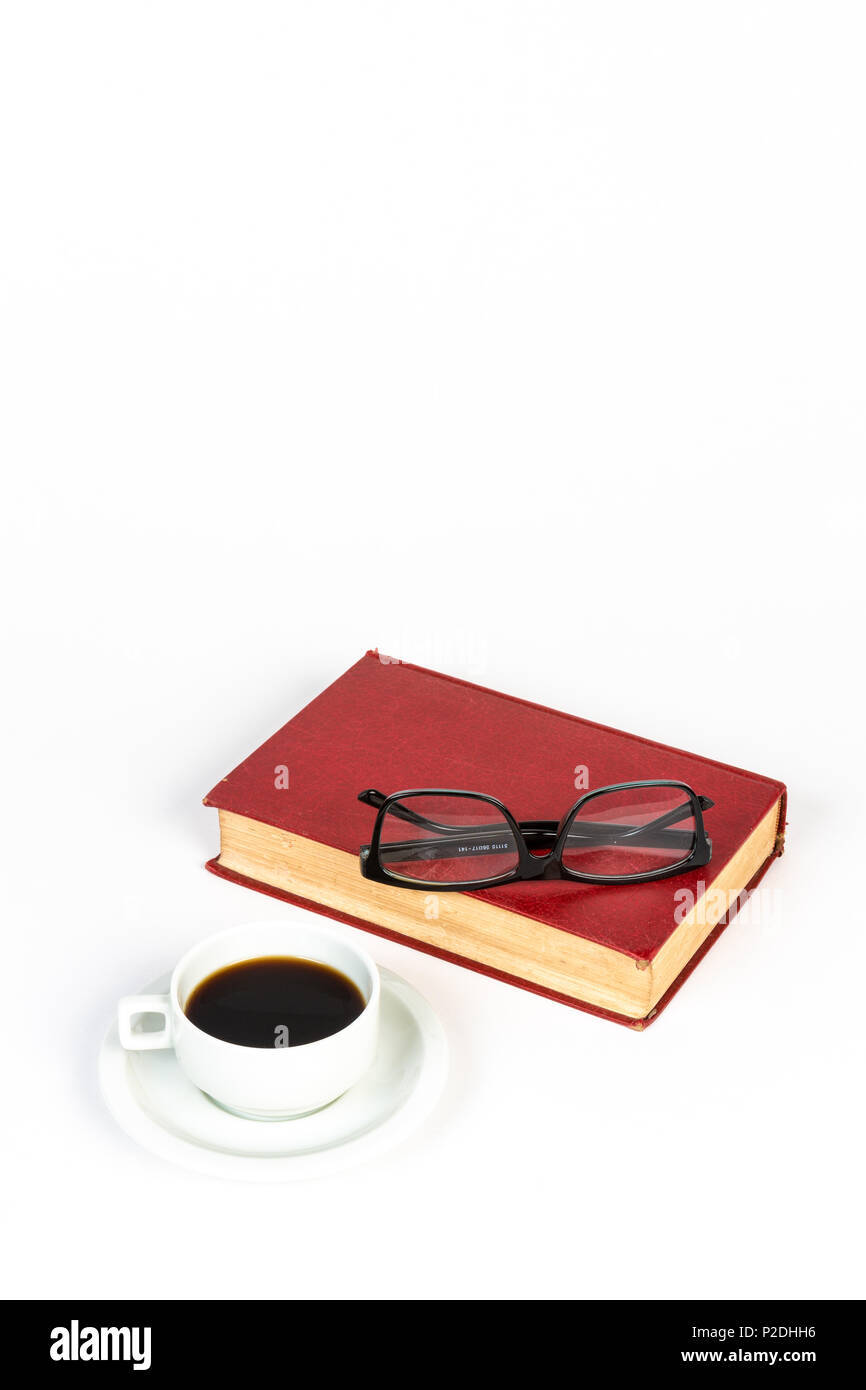 Un livre vintage rouge, une tasse de café, et lunettes noires sur fond blanc. Banque D'Images