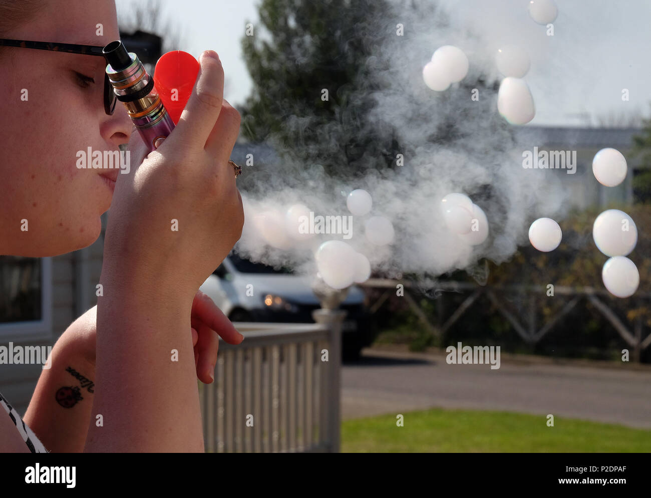 Woman blowing bubbles les remplir de fumée d'une cigarette vaping moderne. Banque D'Images