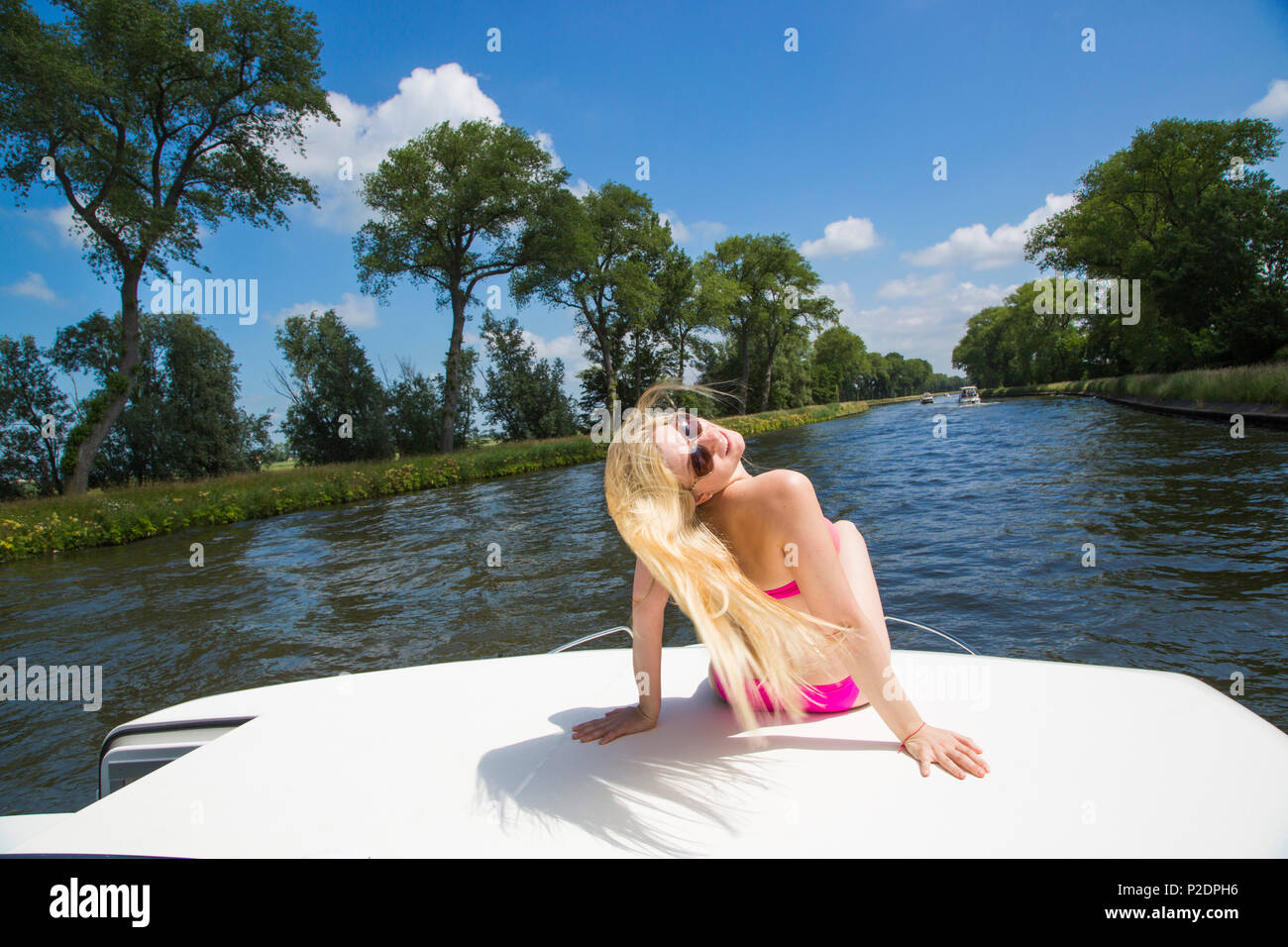 Jeune femme blonde portant un bikini de détente sur le pont d'un bateau péniche Mystique Le Royal sur canal Plassendale - Niuewpoort Banque D'Images