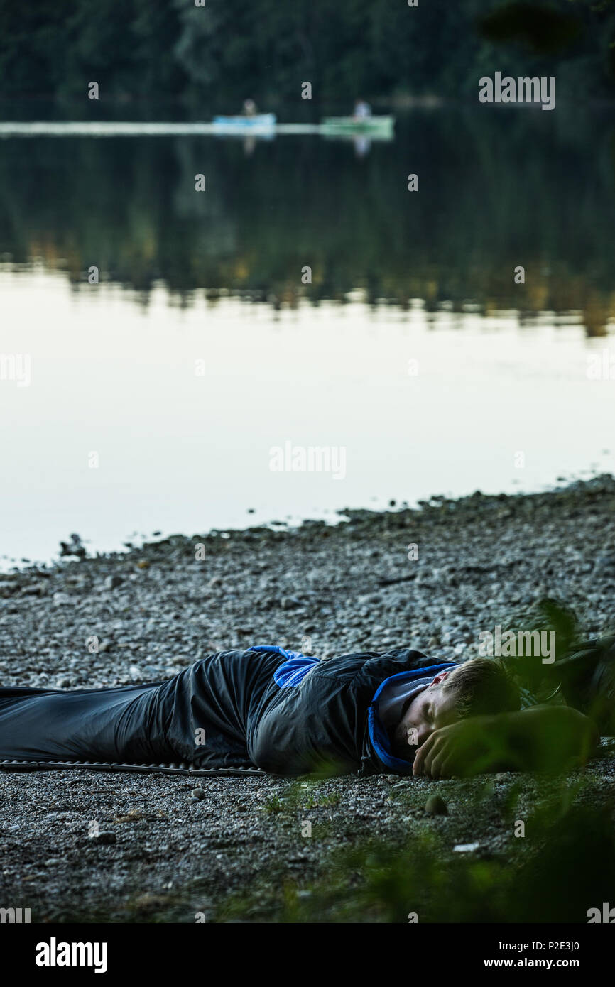 Jeune homme camping à un lac qu'avec un sac de couchage, Freilassing, Bavière, Allemagne Banque D'Images