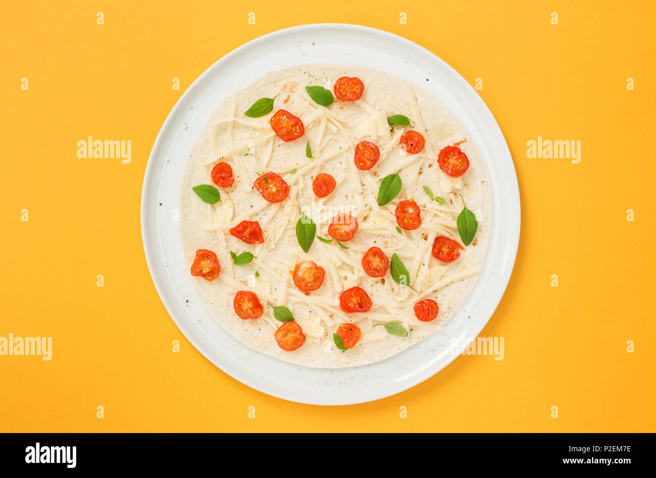 Préparation de tortillas. Tortilla végétarien avec les tomates, le fromage et le basilic, sur fond jaune vif. Banque D'Images