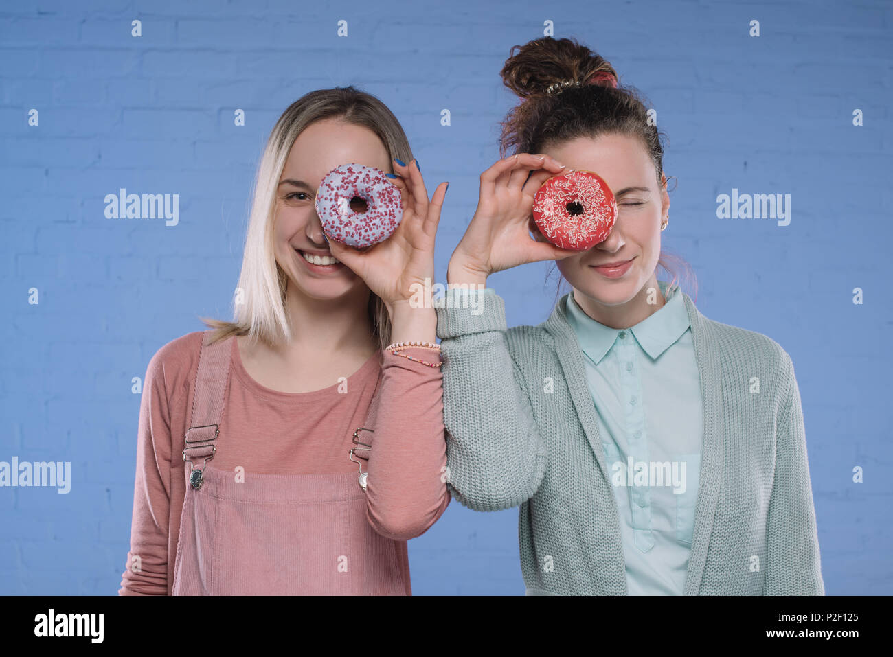 Souriante jeune femme couvrant les yeux avec vitrage donuts Banque D'Images