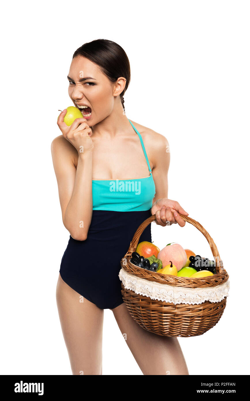 Belle asian woman in swimsuit holding corbeille de fruits tout en mordant, apple isolated on white Banque D'Images