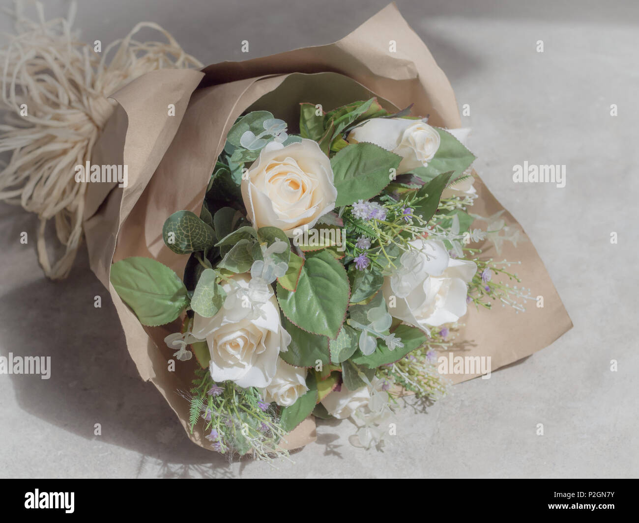 Bouquet de roses blanches artificielles sous emballage papier Craft marron  sur fond de béton Photo Stock - Alamy
