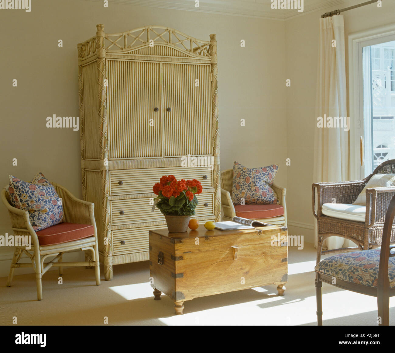 Secrétaire en cabinet et bambou crème poitrine de pin dans coin de chambre ensoleillée avec des fauteuils en rotin avec coussins floraux Banque D'Images