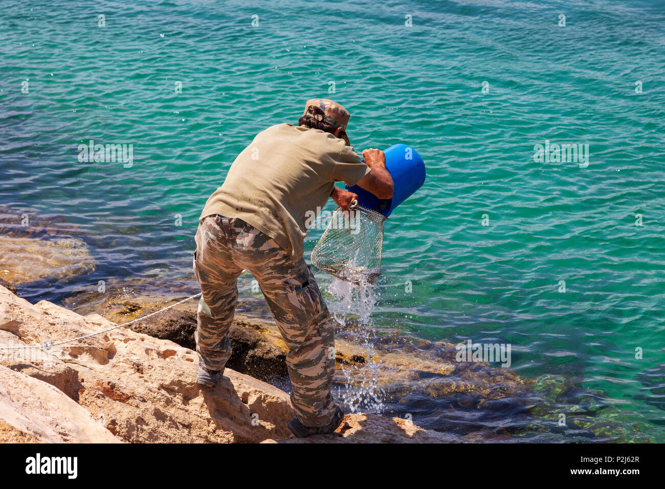 Les pêcheurs de verser l'eau et les poissons qu'il a pris dans un panier métallique pour garder la fraîcheur, Agia Napa, Chypre Banque D'Images