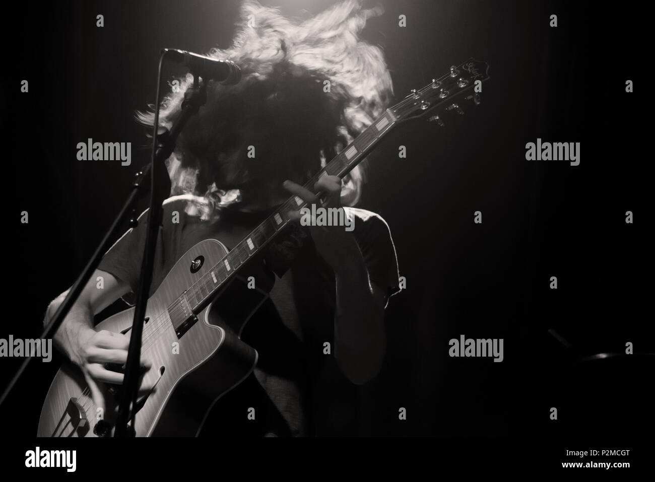Image monochromatique d'un guitariste aux cheveux longs déplace sa tête durant un solo sur scène Banque D'Images