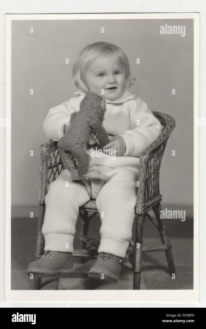 La République socialiste tchécoslovaque - Vers les années 1970 : Vintage photo montre une petite fille est assise sur chaise en osier et peluche détient (animal en peluche). Retro noir et blanc de la photographie. Banque D'Images