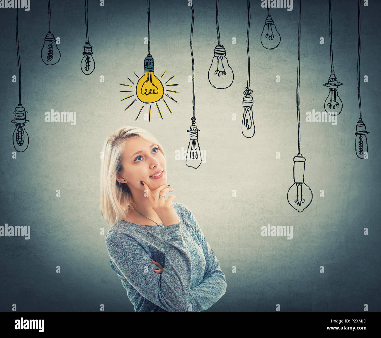 Portrait of young woman looking up à une ampoule incandescent accroché à un fil, alors que les autres sont hors tension. La planification de projet d'entreprise con Banque D'Images