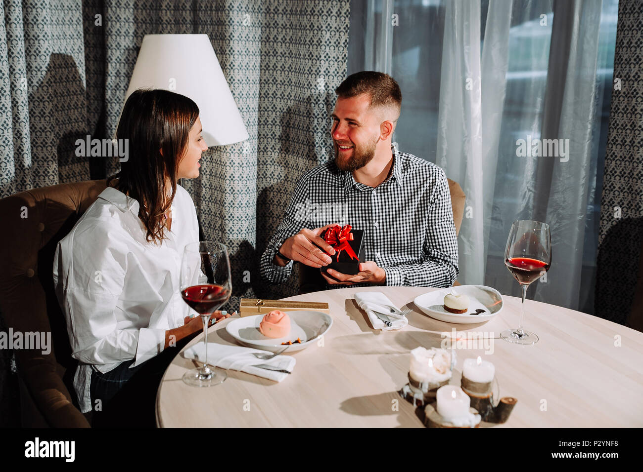 Un homme ouvre une boîte-cadeau à une date.side view portrait of laughing couple enjoying date in cafe Banque D'Images