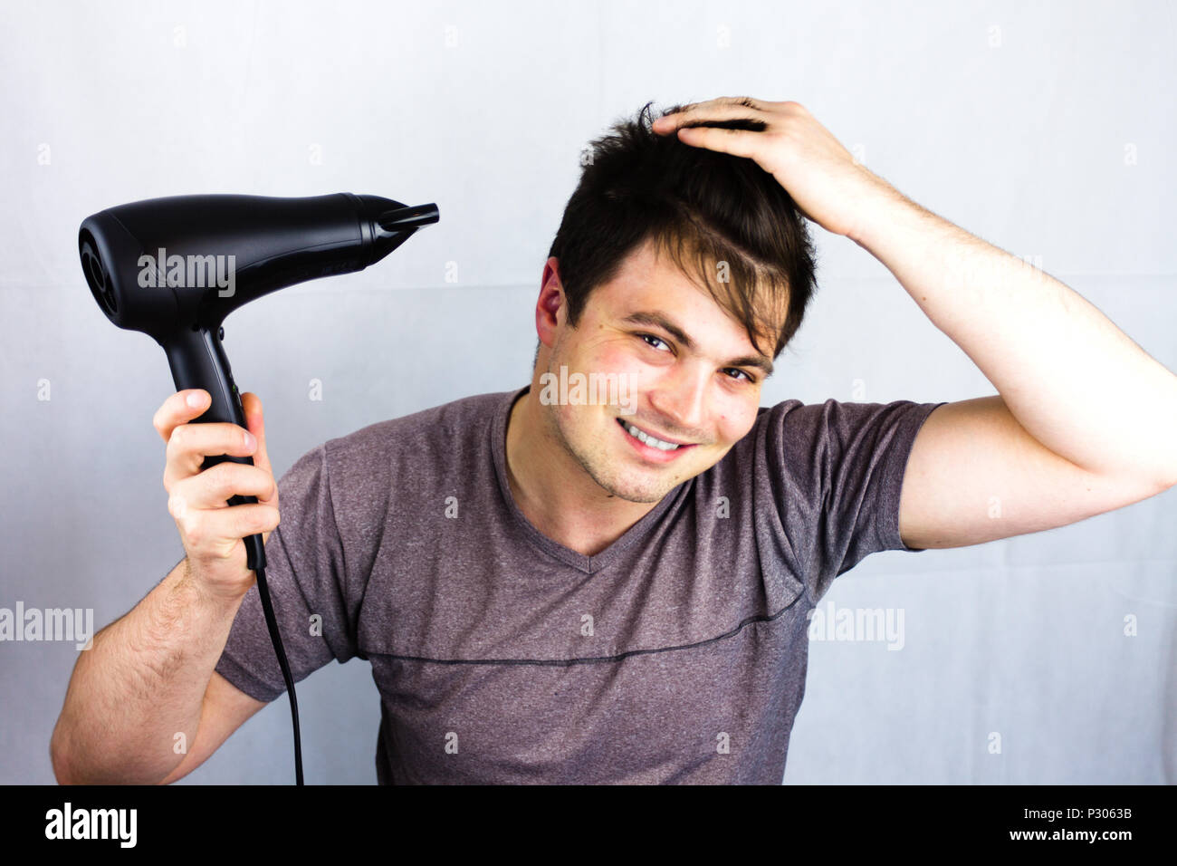 Jeune homme sèche cheveux avec un ventilateur électrique. La préparation  d'une coupe pour aller à une vie nocturne.Man holding sèche-cheveux.  Smiling adolescent alors qu'il sèche sa Photo Stock - Alamy