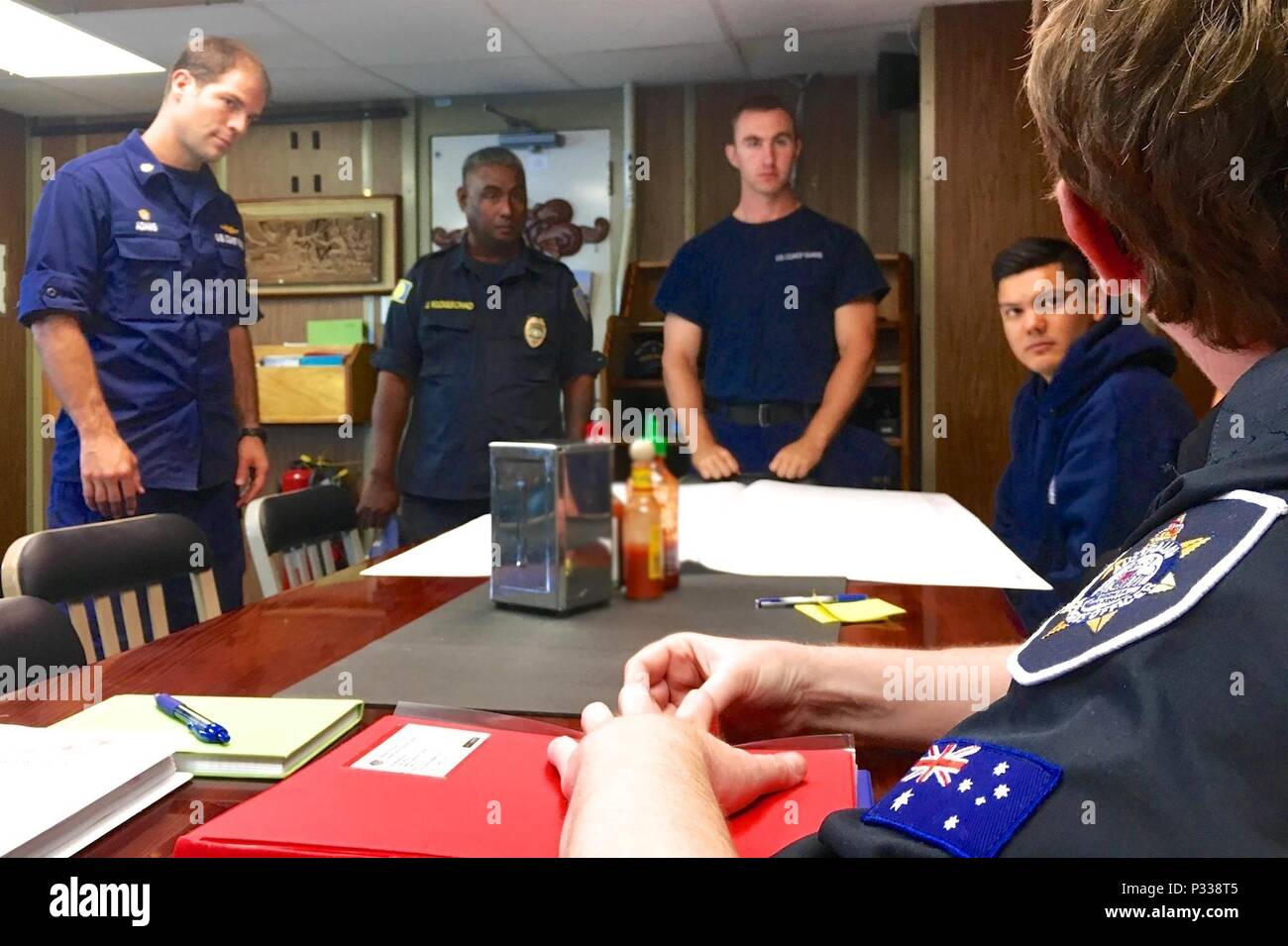 Le lieutenant Cmdr. William Adams, commandant de la WLB-215 USCGC (Sequoia), Jim Kloulechad Palau, Police nationale, Ensign Luc Trautwein et le lieutenant J.G. Charlie Trotten, officier des opérations, écouter une liste des récentes violations observées par le personnel de l'Agence de gestion des pêches de l'Australie au cours de l'arraisonnement en haute mer donnée par Lydia Woodhouse shiprider à bord de l'AFMA un Sequoia pendant qu'ils sont en cours dans l'océan Pacifique le 30 août 2016. Les partenaires de la Garde côtière des États-Unis avec l'AFMA d'élargir sa compétence et les autorités à mener des inspections à la zone de la haute mer Banque D'Images