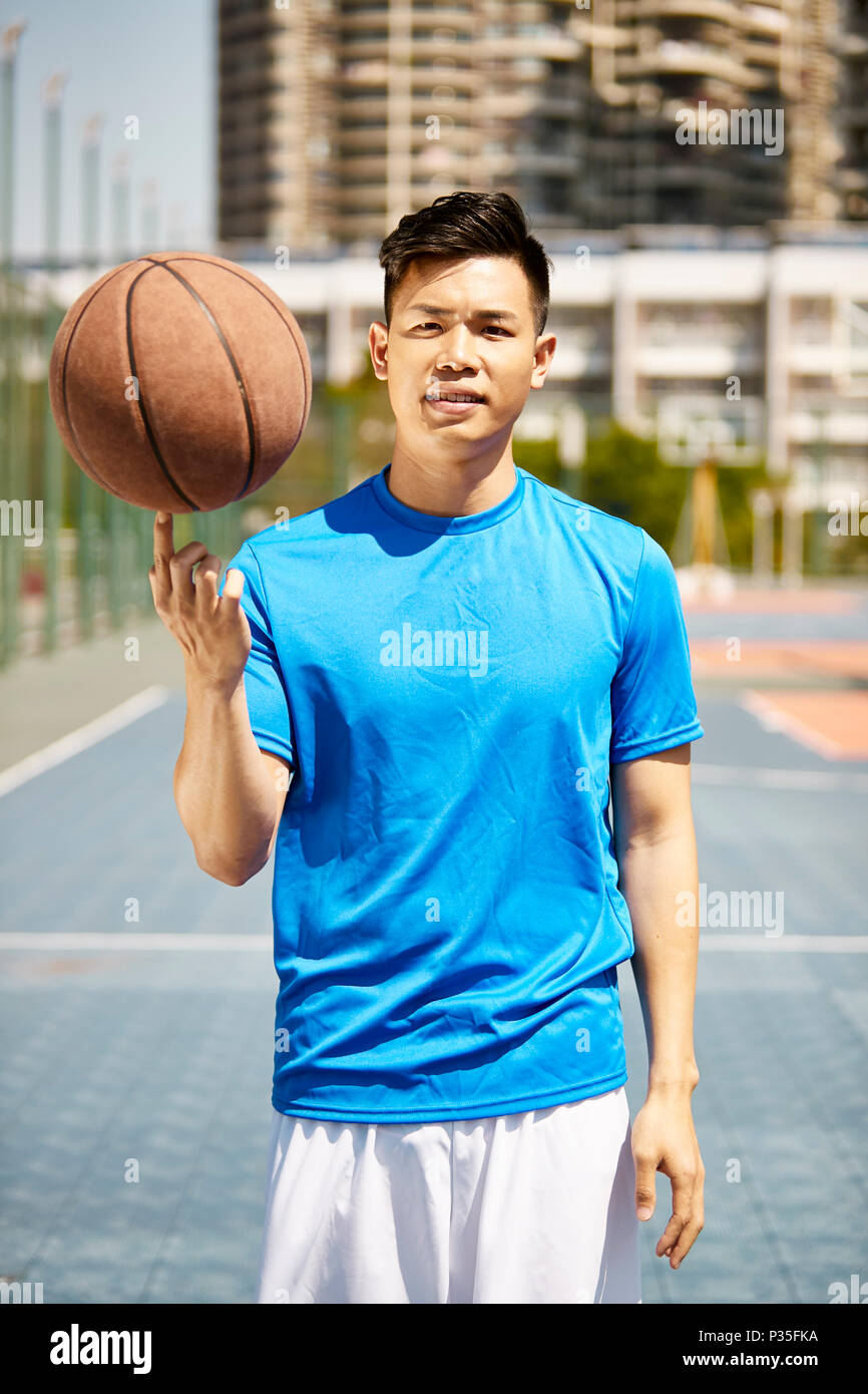 Young Asian man holding a basket-ball sur le doigt à la recherche à l'appareil photo. Banque D'Images