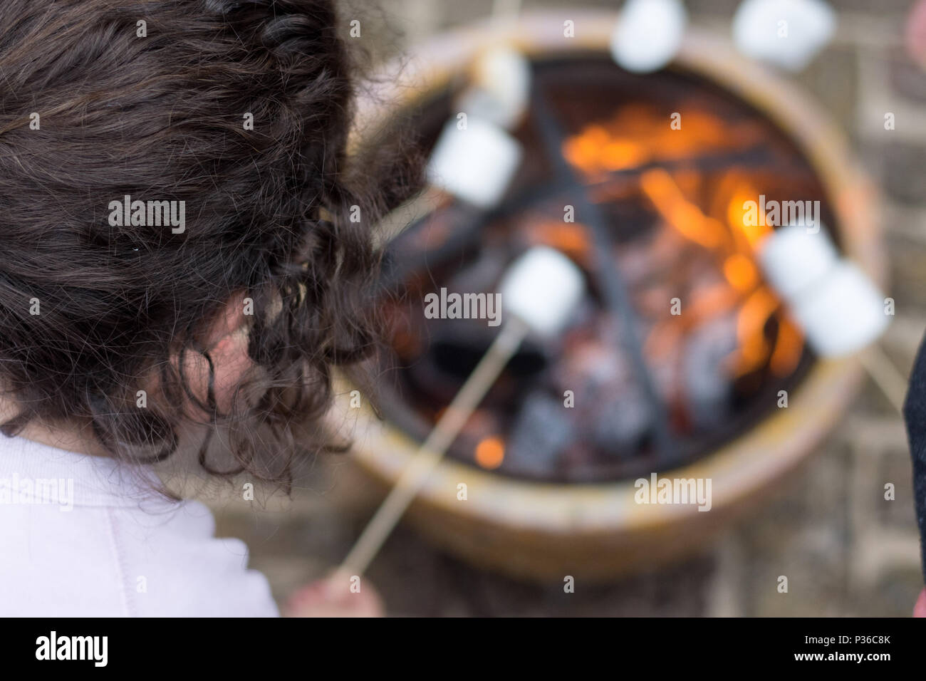 Girl toasting mash mallows sur open fire pit at garden party Banque D'Images