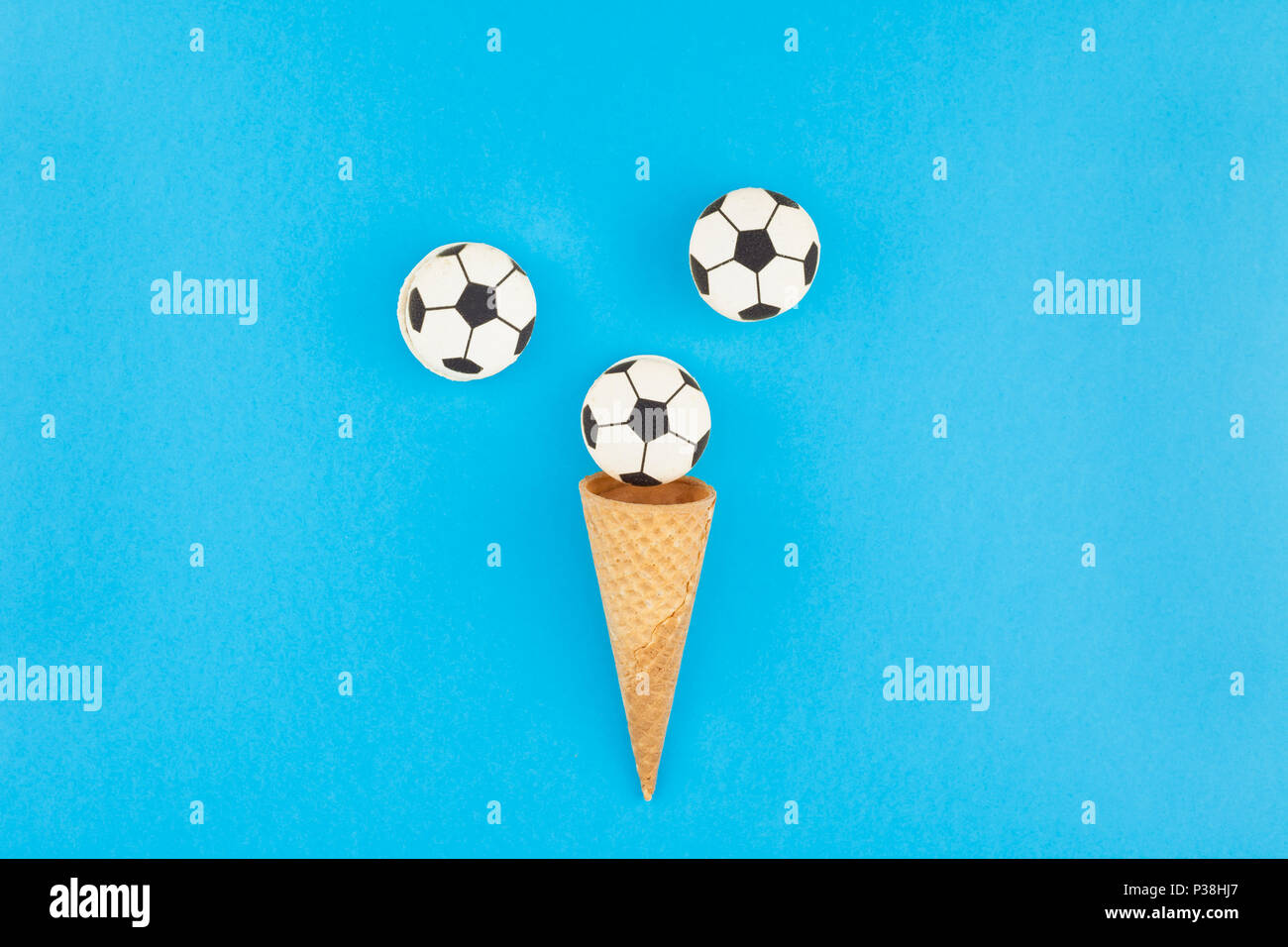 Télévision créative jeter Vue de dessus de la crème glacée cônes alvéolés avec des ballons de foot macarons sur fond bleu clair bold avec copie espace dans un style minimaliste, conce Banque D'Images