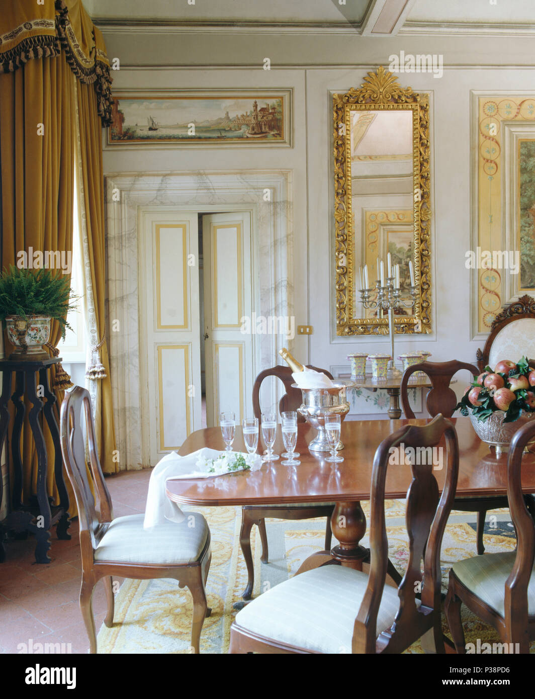 Chaises anciennes à table dans la salle à manger de la Toscane avec un miroir ancien doré sur le mur près de la porte double Banque D'Images