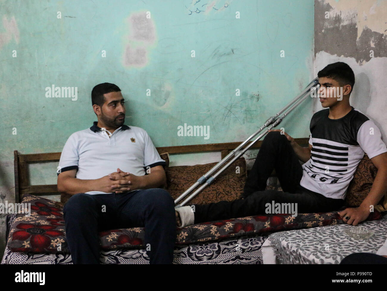 La ville de Gaza, en Palestine. 16 Juin, 2018. Ahmed s'assit avec son ami dans sa maison à al-Bureij camp de réfugiés, le deuxième jour de l'Aïd al-Fitr, célébrée par les musulmans.Ahmed Jawad Mahmoud Othman a 19 ans, les jeunes Palestiniens d'al-Bureij camp de réfugiés dans le sud de la bande de Gaza a été tué par balle à la jambe gauche par des balles réelles au cours d'affrontements entre les civils palestiniens et soldats israéliens sur la frontière de la bande de Gaza à l'est de al-Boreij camp de réfugiés à une protestation du président américain la reconnaissance de l'Atout de Jérusalem comme capitale d'Israël. Et le transfert de l'ambassade américaine à Jérusalem. (Crédit Image : © Ahmad Hasab Banque D'Images