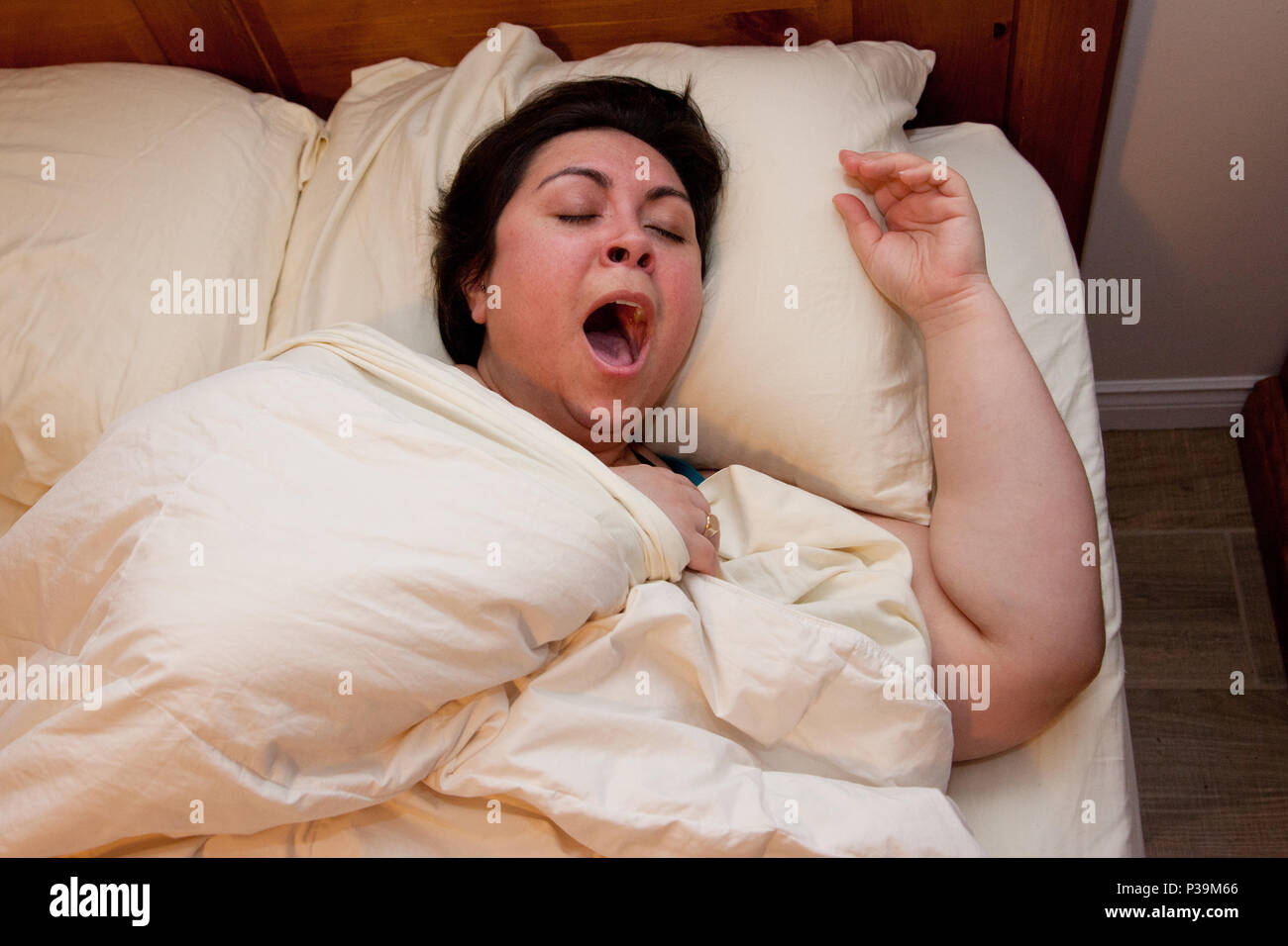 Une femme est blotti sous les couvertures avec un grand bâillement Banque D'Images