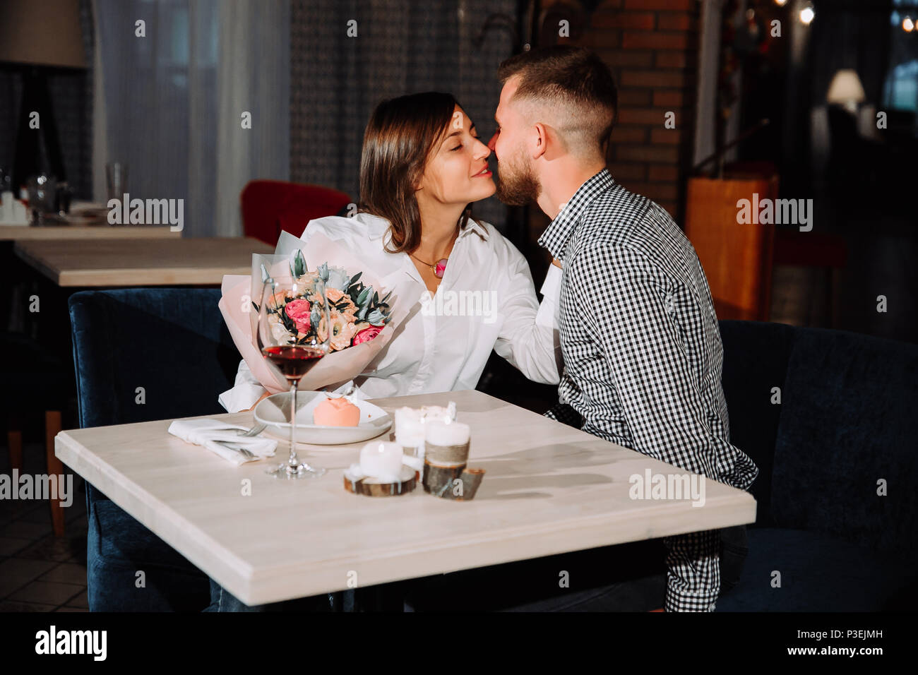 Heureux couple romantique dans le café. Jeune homme présente des fleurs à sa bien-aimée. Banque D'Images