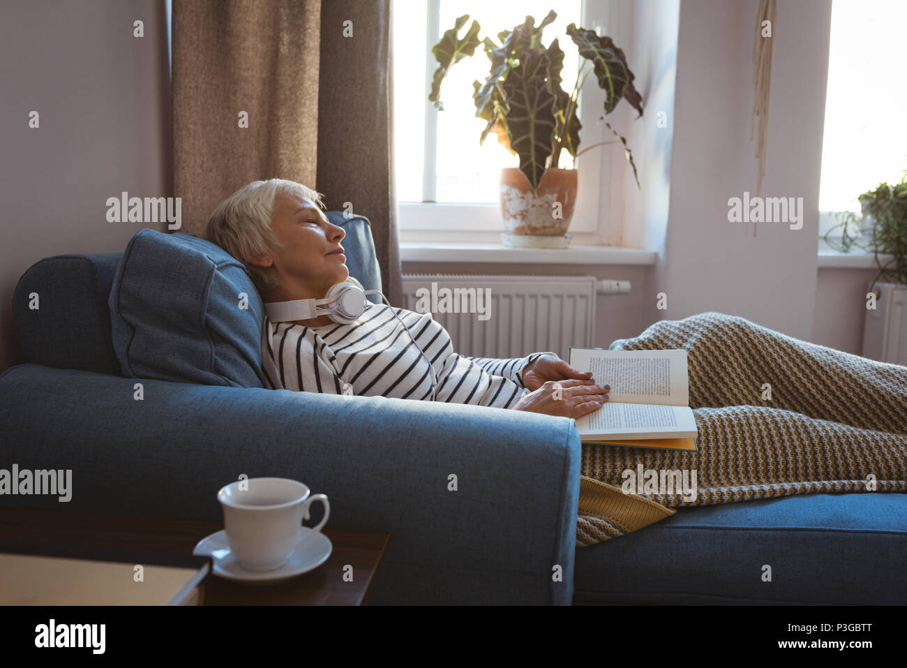 Senior woman prendre une sieste sur le canapé tandis que la lecture du livre dans la salle de séjour Banque D'Images