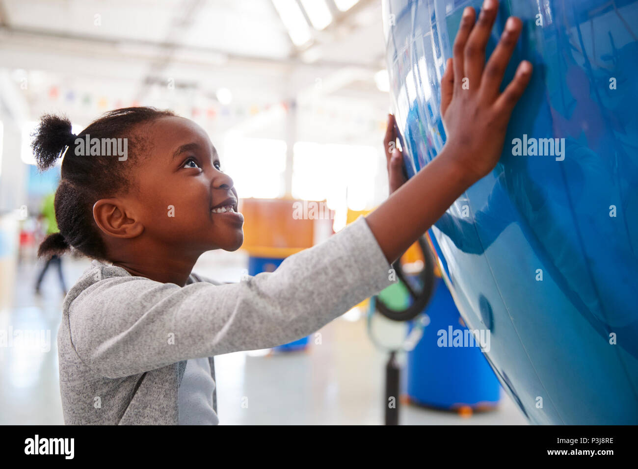Jeune fille noire tenant un globe géant dans un centre des sciences Banque D'Images
