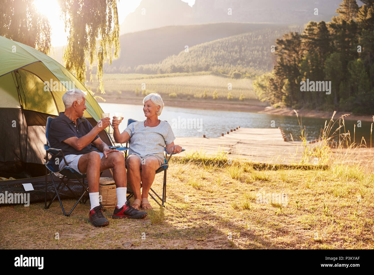 Senior Couple Enjoying Camping Locations par le lac faire un toast Banque D'Images