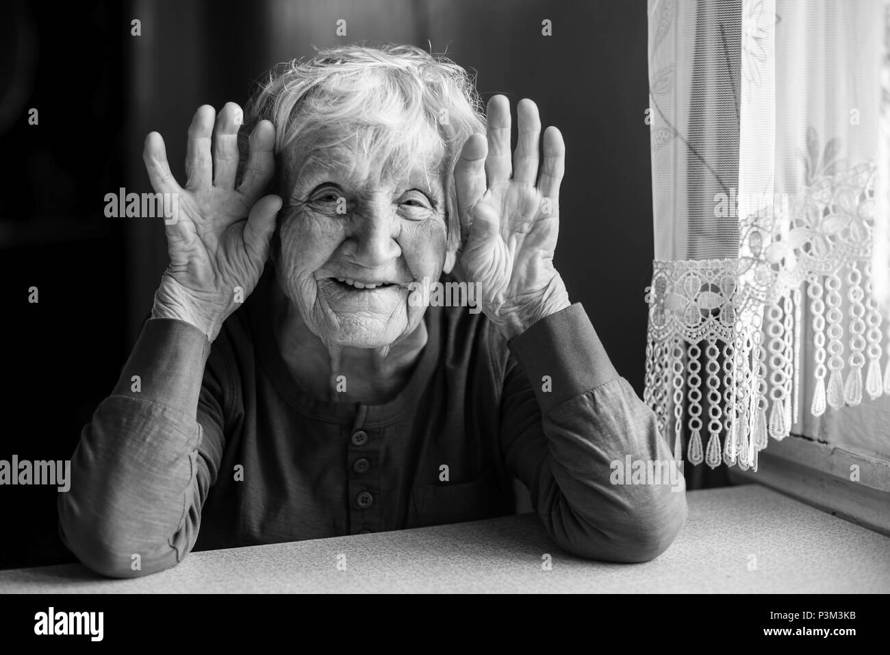 Portrait of smiling woman holding vieille ridée mains près de ses oreilles. Photo en noir et blanc. Banque D'Images