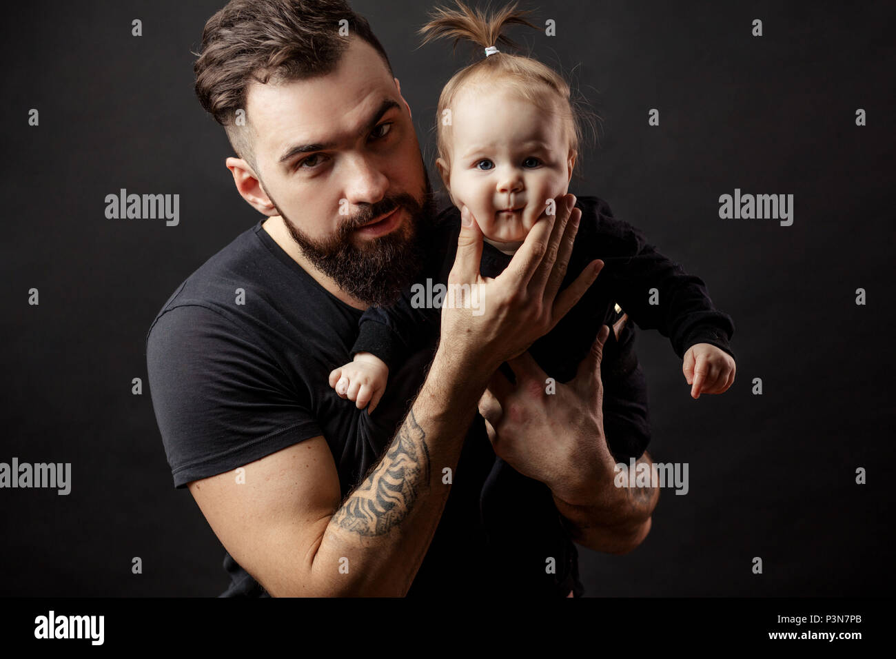 Jeune père athlétique avec bébé adorable sur fond noir Banque D'Images