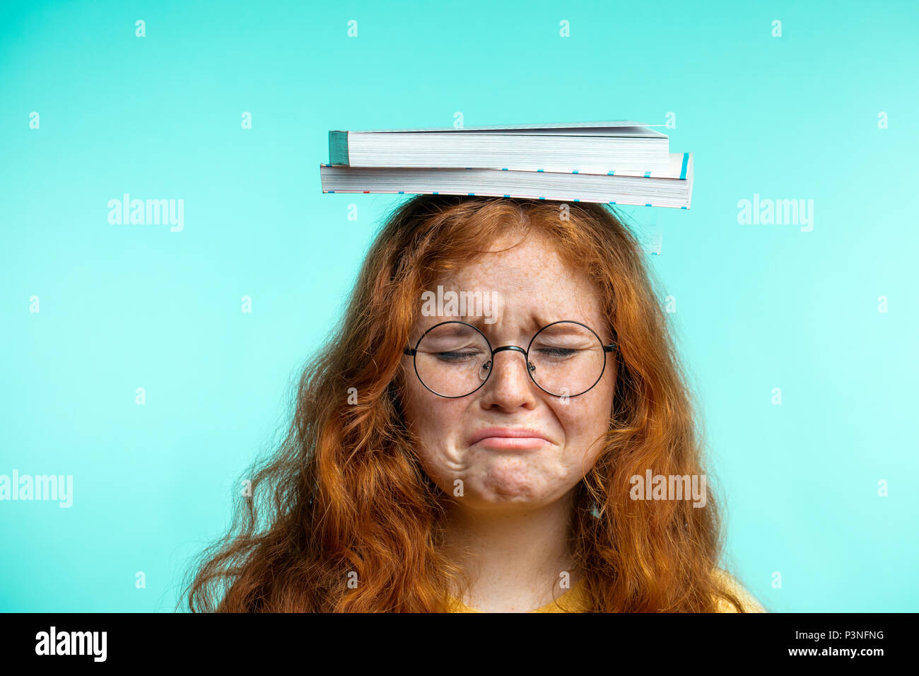 Portrait d'adolescente frustrée transportant sur la tête livre isolé sur blue Banque D'Images