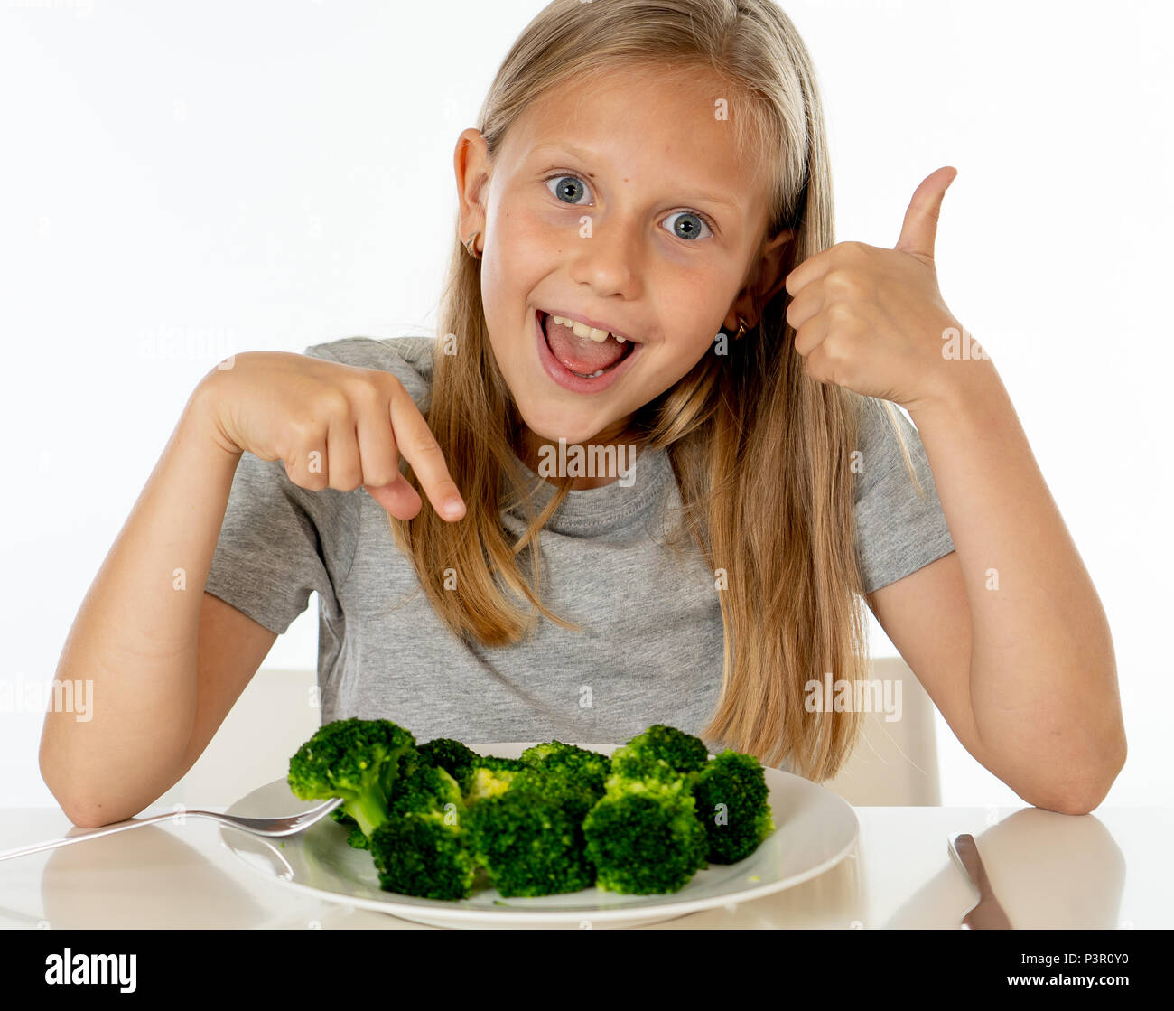 Jeune fille blonde with Thumbs Up à les apprécier et aimer manger son légumes brocoli sur une plaque avec couteau et fourchette dans les enfants en bonne santé de manger co Banque D'Images