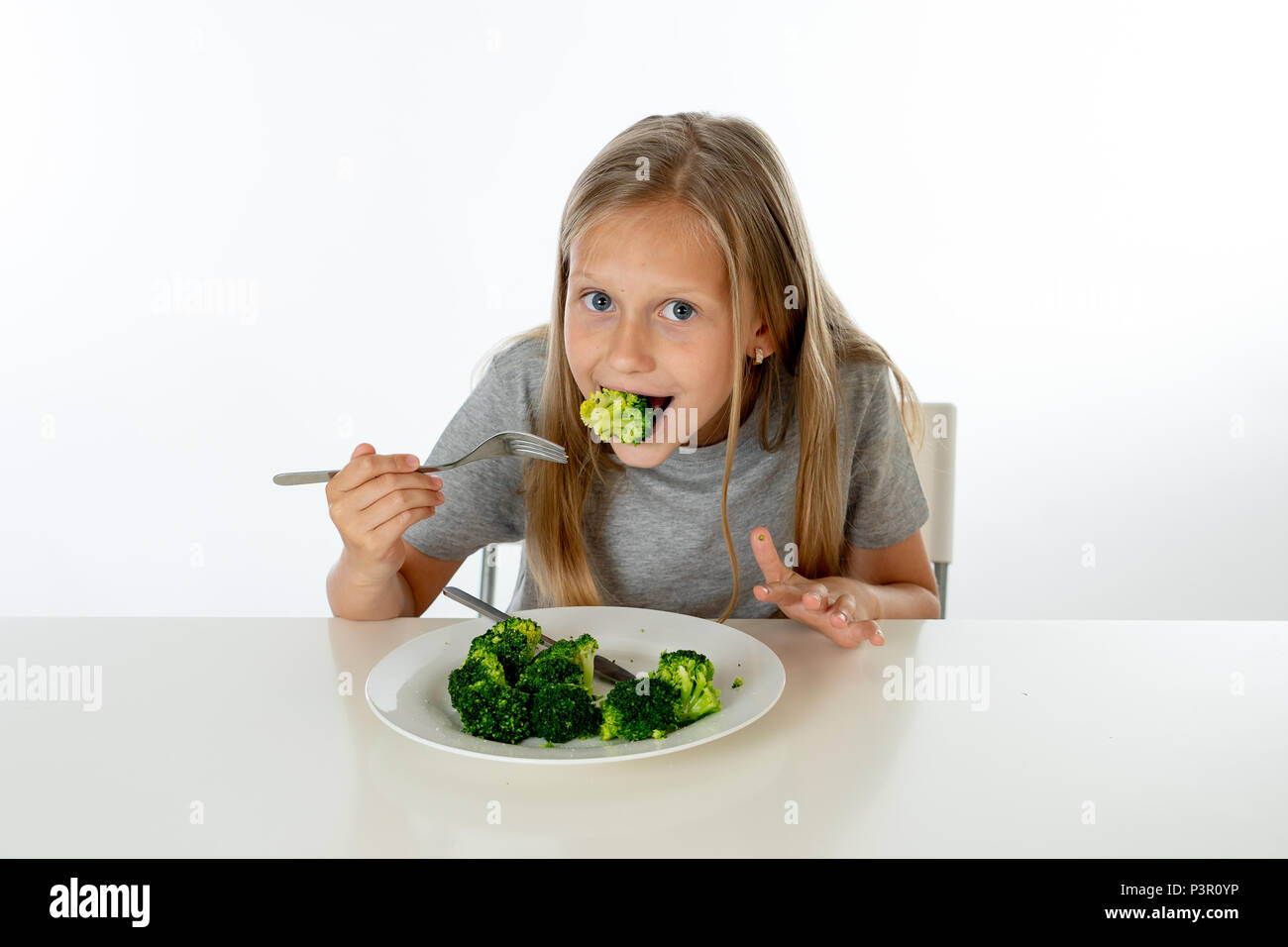 Jeune fille blonde with Thumbs Up à les apprécier et aimer manger son légumes brocoli sur une plaque avec couteau et fourchette dans les enfants en bonne santé de manger co Banque D'Images