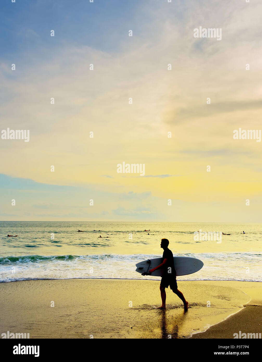 Surfer avec une planche de surf à pied sur la plage au coucher du soleil. L'île de Bali, Indonésie Banque D'Images