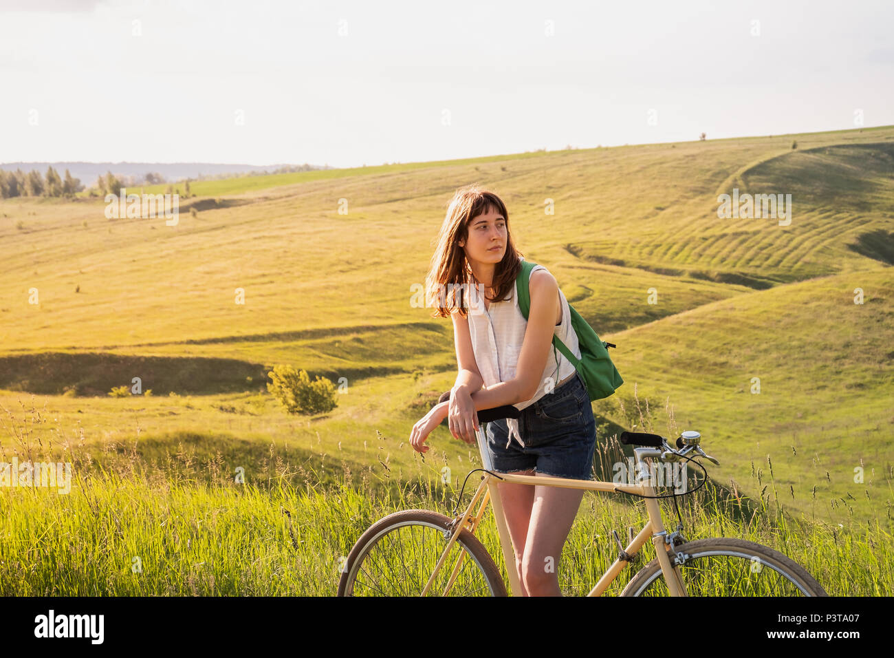 Fille avec location dans un beau cadre rural au coucher du soleil. Jolie jeune femme avec vélo rétro dans un pré sur l'après-midi ensoleillée dans Banque D'Images