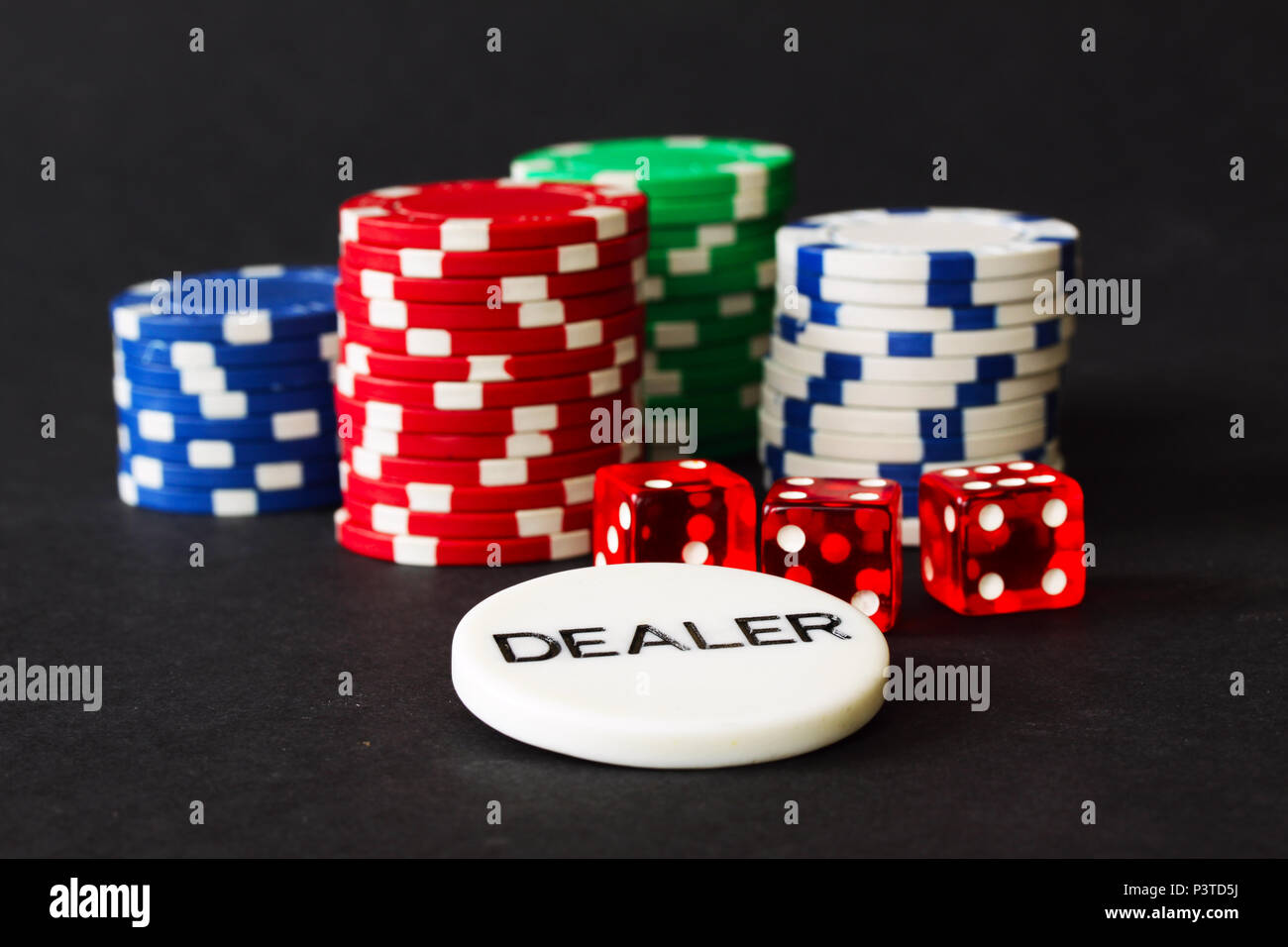 Des jetons de poker et Red Dice avec badge revendeur en premier plan et arrière-plan noir Banque D'Images