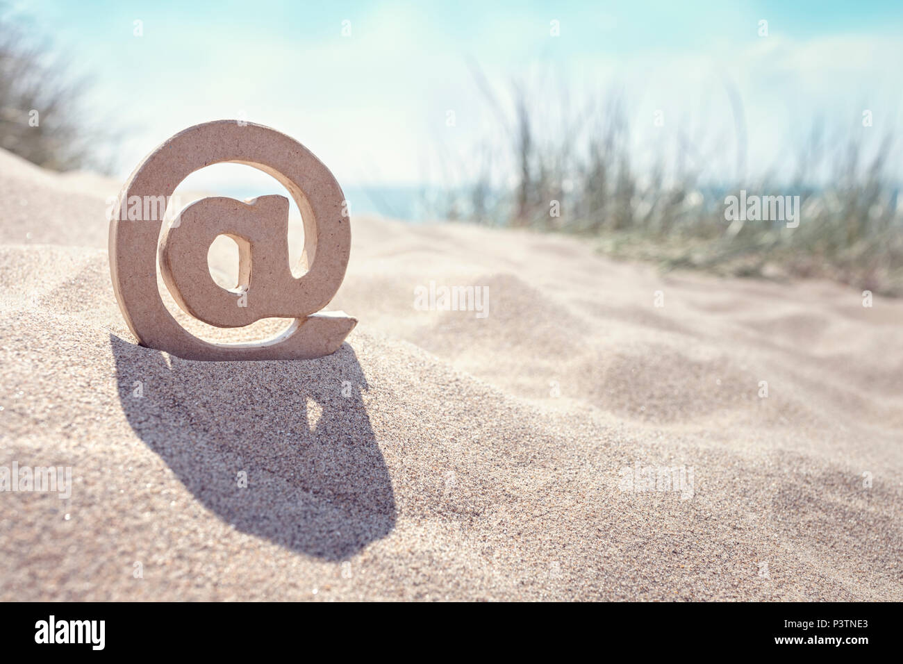 Email @ symbole dans le sable à la plage Banque D'Images