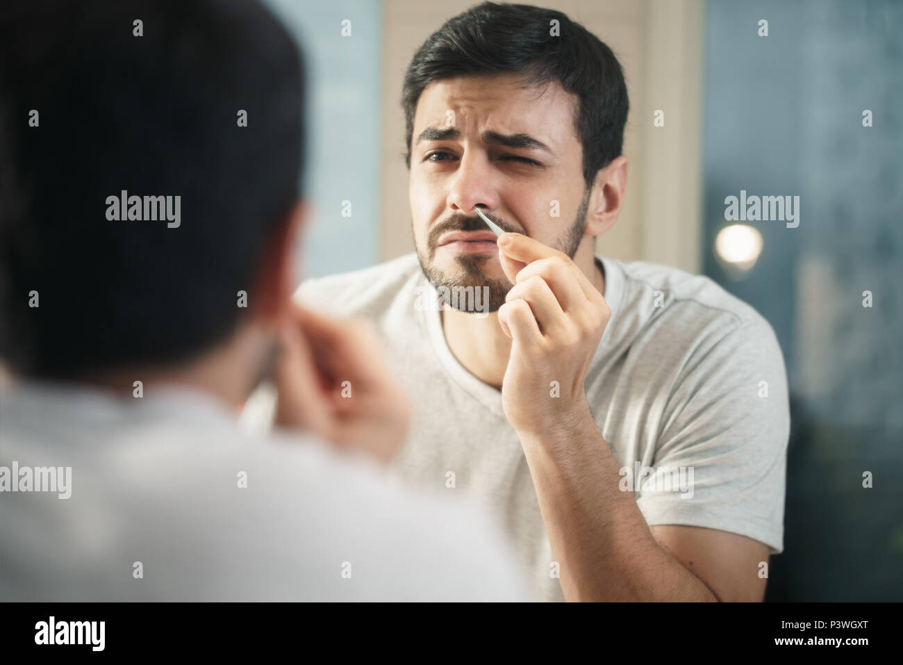 Bel homme parage les poils du nez dans la salle de bains Banque D'Images