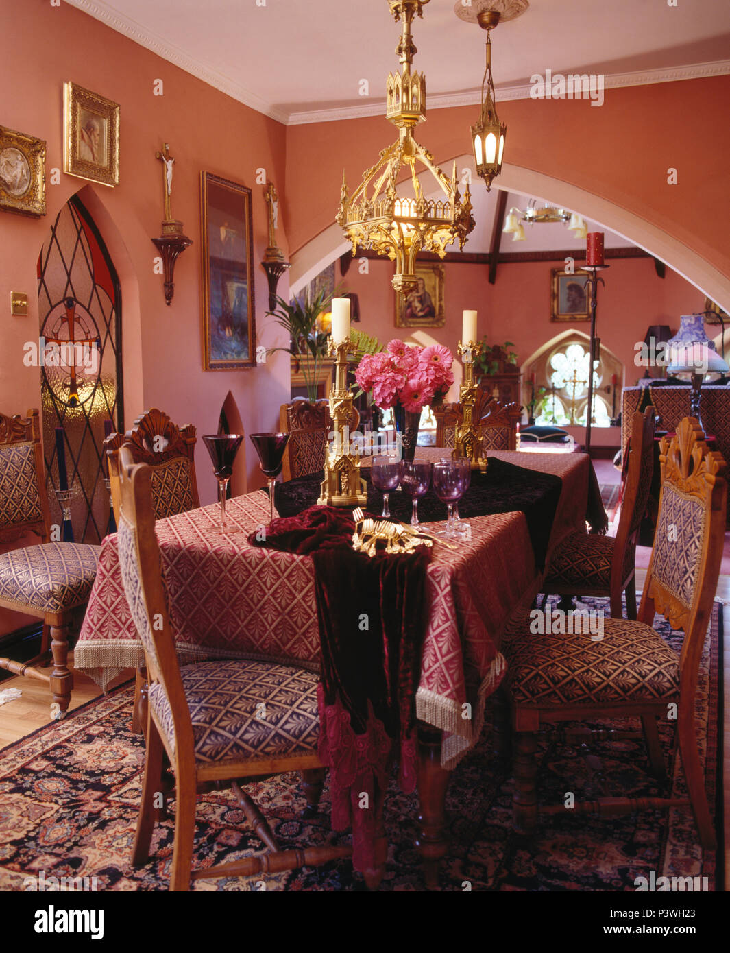 Salle à manger en chapelle convertie avec lampes en laiton au-dessus de table avec du tissu à motifs rouge foncé et de chaises assorties Banque D'Images