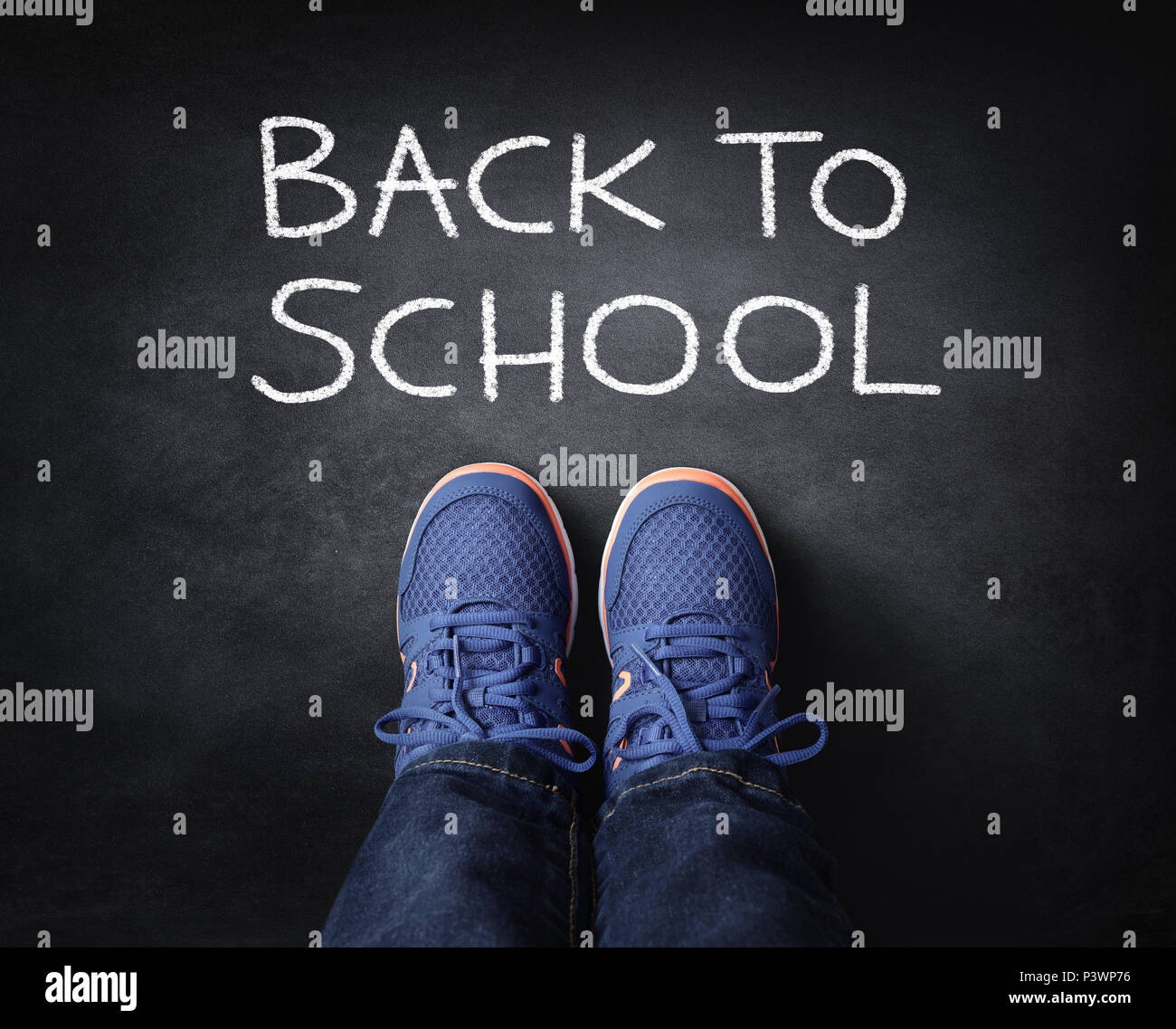 Retour à l'école enfant dans sneakers debout à côté de l'écriture à la craie sur tableau noir Banque D'Images