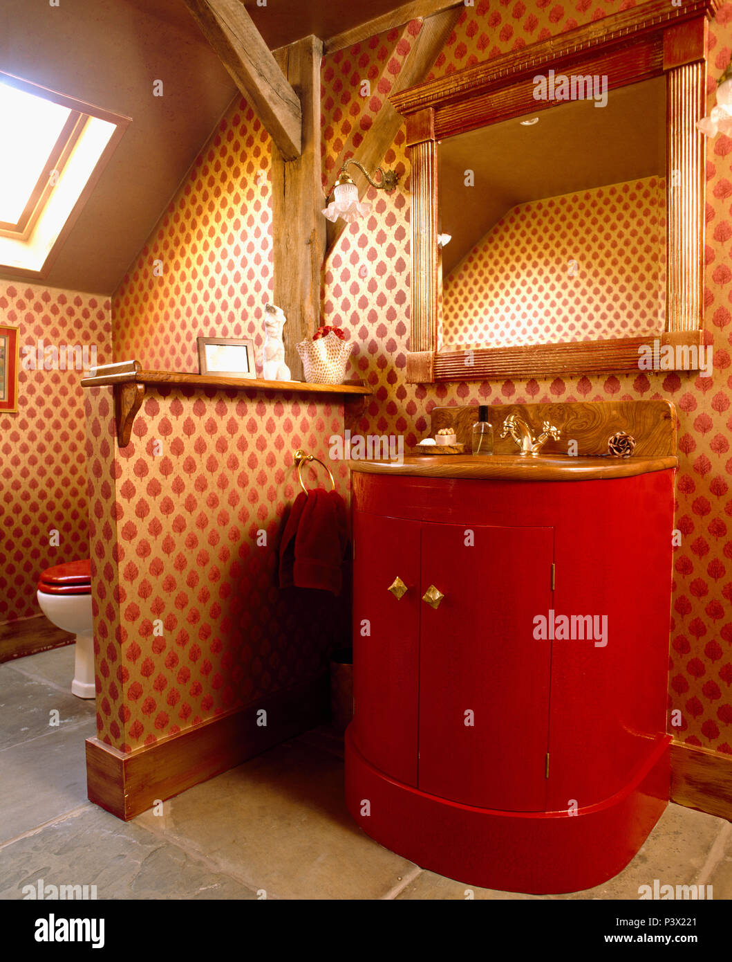 La moitié mur entre toilettes et du lavabo dans salle de bains mansardée avec papier peint à motifs rouge et miroir doré Banque D'Images