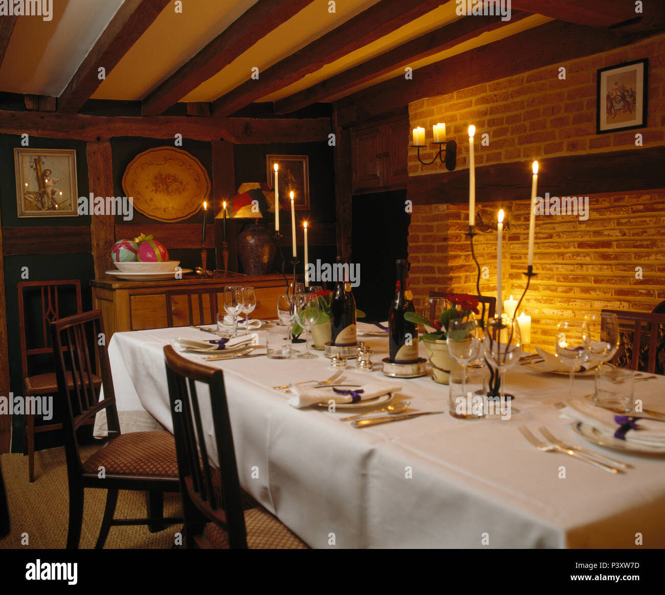 Des draps blancs et des bougies allumées sur le set de table pour le dîner dans la salle à manger pays avec poutres apparentes Banque D'Images
