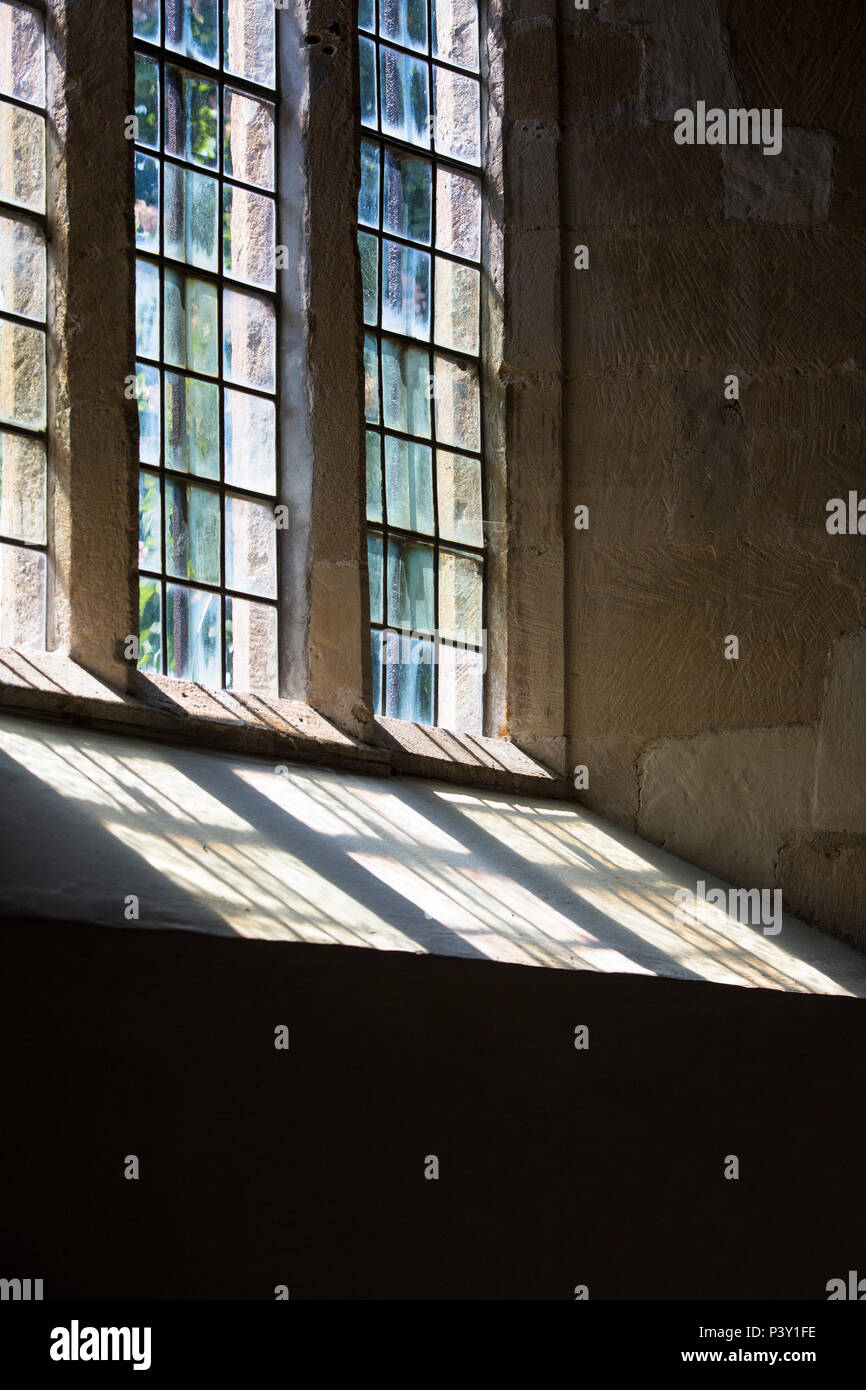 Une vieille fenêtre au plomb planer une menace et l'ensemble de la lumière des murs en pierre d'une église. Banque D'Images