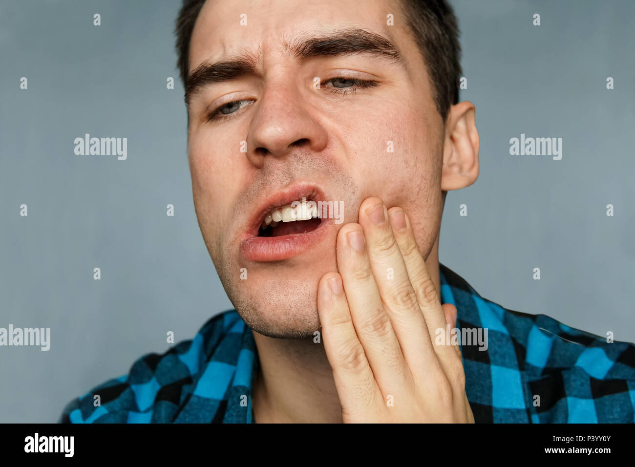 Un jeune homme avec une rage de dents sur un fond bleu. Le gars avec le mal de jaw détient l'arrière de sa gorge Banque D'Images