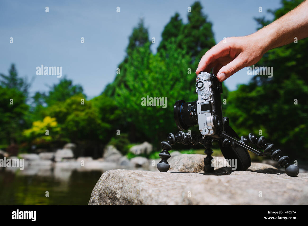 Homme Photo manipulation à la main un vieux millésime caméra sur trépied en face de l'eau étang parc Planten un Blomen à Hambourg, Allemagne Banque D'Images