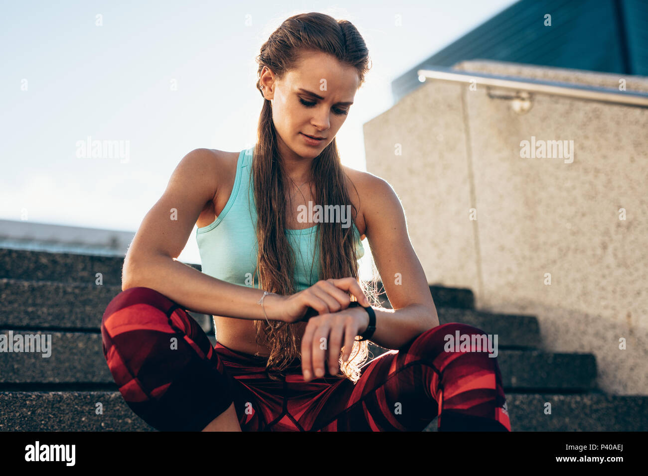 Fit young woman sitting on stairs et regardant sa montre intelligente à l'extérieur. Contrôle de l'athlète féminine de l'app dans sa smartwatch remise en forme après l'entraînement. Banque D'Images