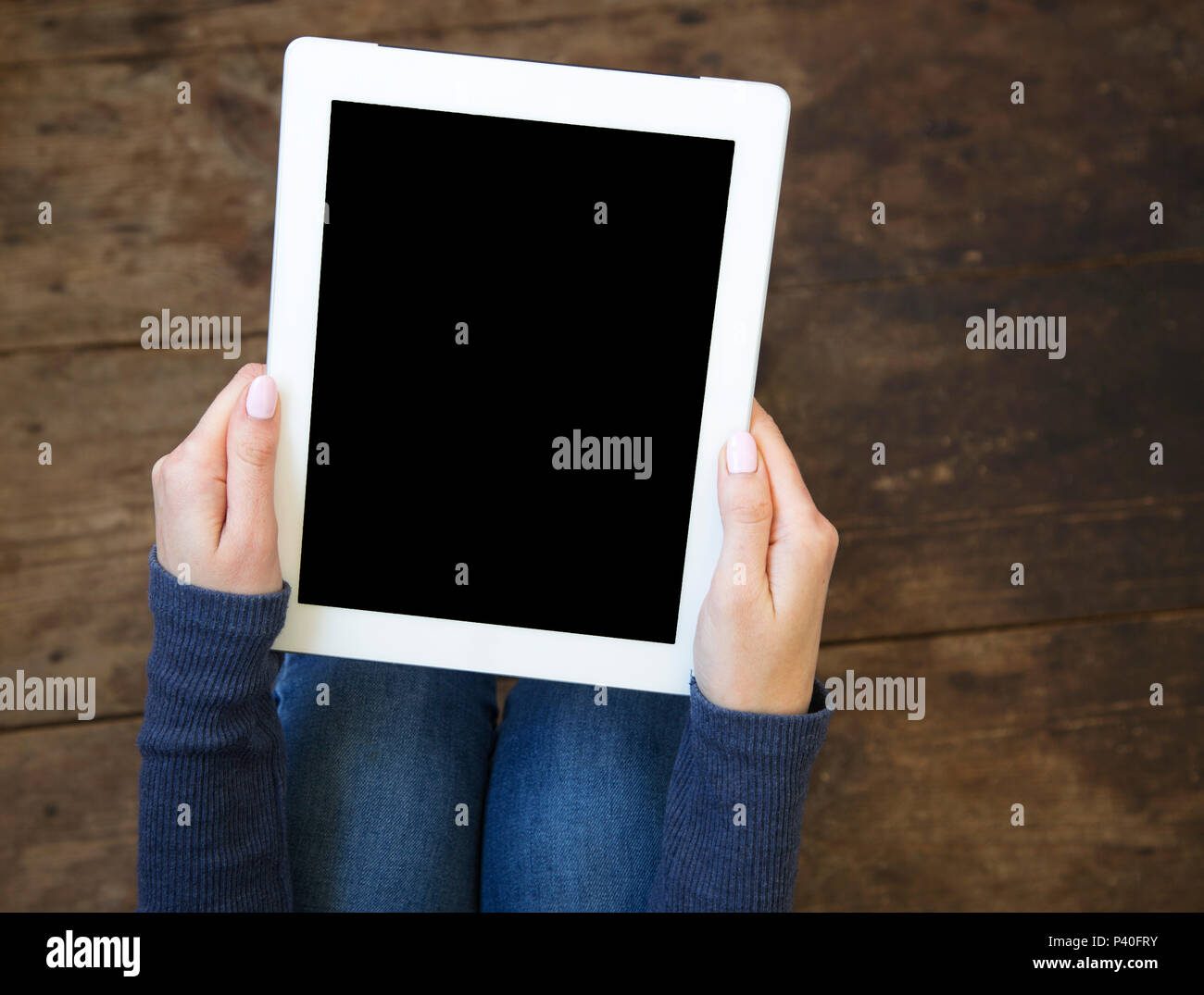 La jeune fille est assise sur un sol en parquet et est titulaire d'une tablette avec un écran vide dans ses mains. Vue d'en haut. Banque D'Images