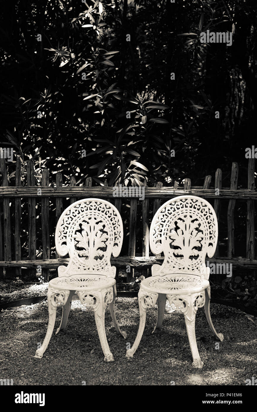 Une cour extérieure avec une paire de chaises anciennes blanches en fer forgé qui attendent apparemment le retour de quelqu'un Banque D'Images