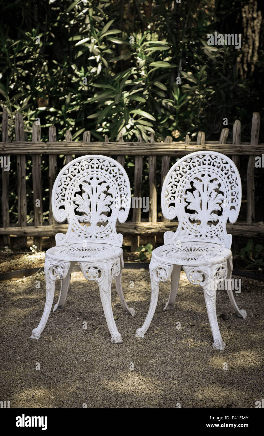 Une cour extérieure appréciable avec une paire d'anciens vides chaises blanches en fer forgé en attente de retour de quelqu'un apparemment Banque D'Images