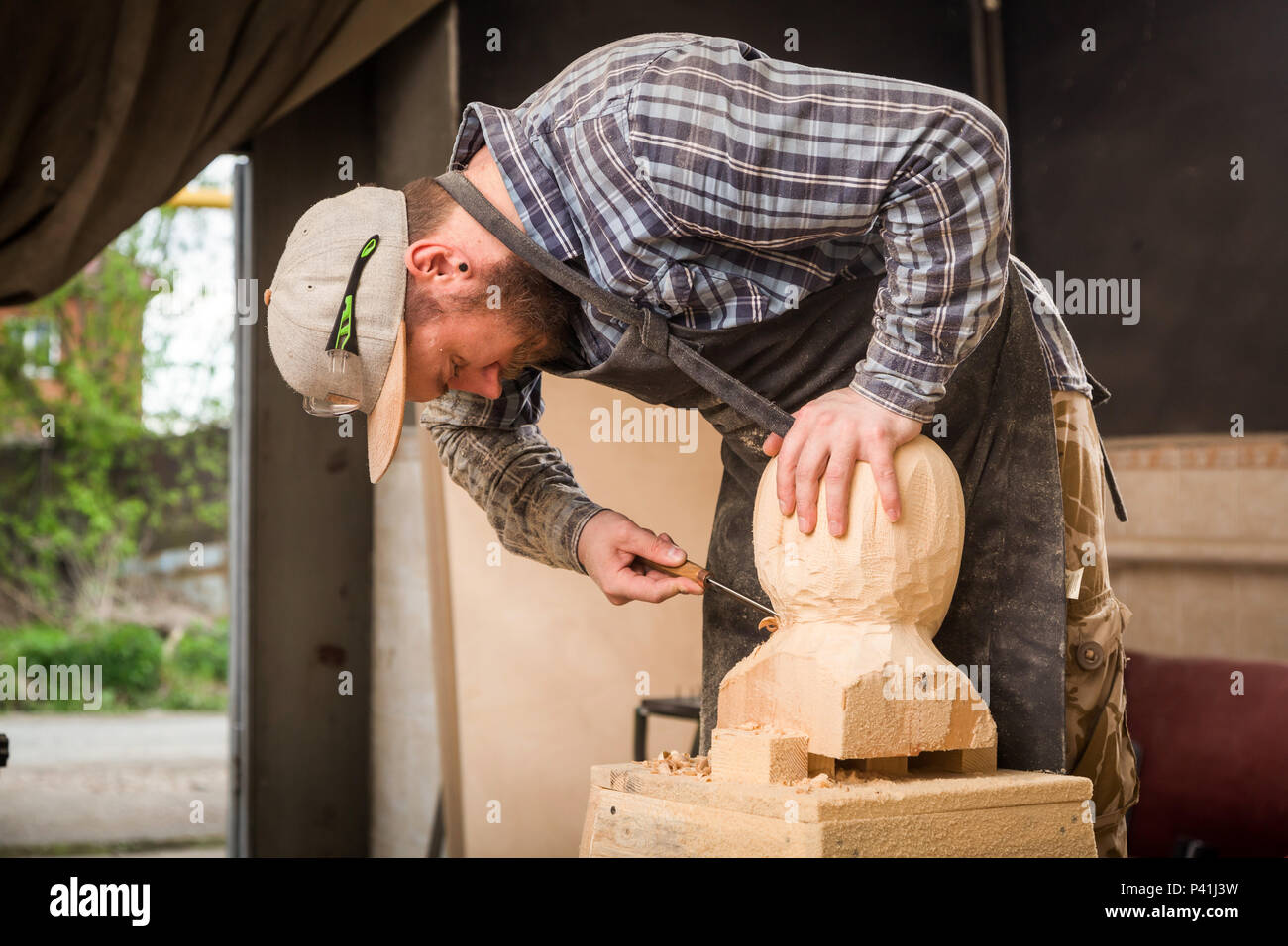 Jeune homme dans un menuisier scies vêtements de travail à la tête d'un homme avec un arbre , à l'aide d'un burin dans l'atelier, autour d'un lot d'outils pour le travail Banque D'Images